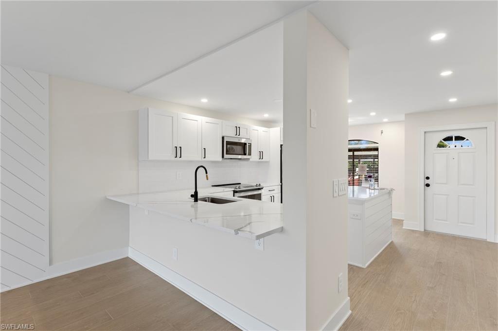Kitchen with light wood-type flooring, light stone countertops, white cabinetry, a peninsula, and recessed lighting