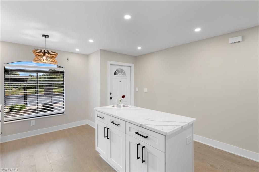 Kitchen featuring decorative light fixtures, white cabinets, a center island, recessed lighting, and light stone countertops