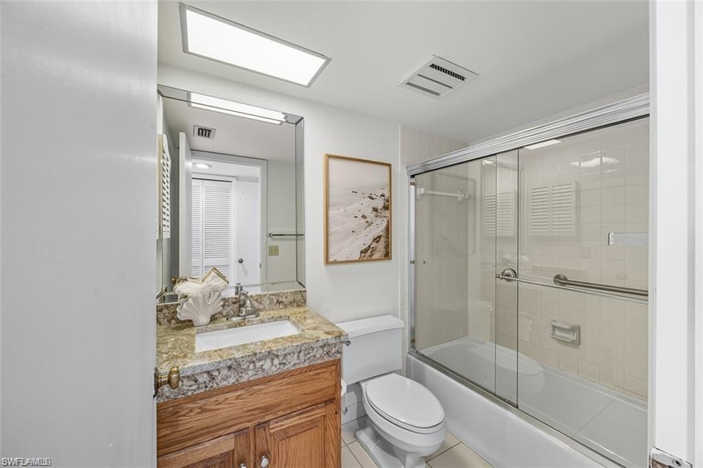Bathroom featuring vanity, bath / shower combo with glass door, and light tile patterned floors
