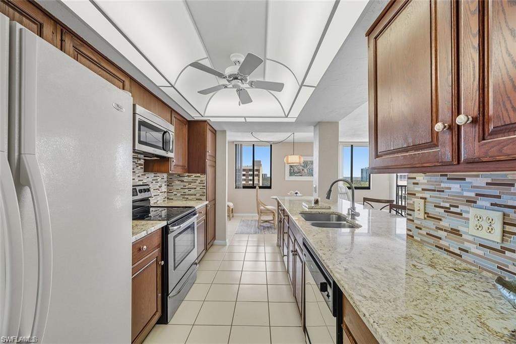 Kitchen featuring appliances with stainless steel finishes, backsplash, light stone counters, light tile patterned floors, and a tray ceiling