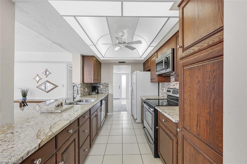 Kitchen featuring appliances with stainless steel finishes, light stone countertops, tasteful backsplash, a tray ceiling, and light tile patterned floors
