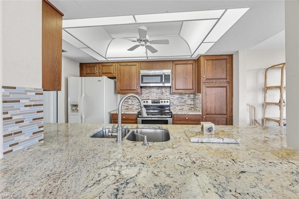 Kitchen with brown cabinets, backsplash, stainless steel appliances, and light stone counters