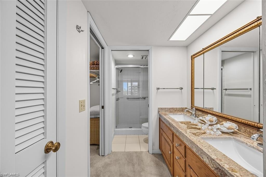 Ensuite bathroom featuring a closet, double vanity, a shower stall, and light colored carpet
