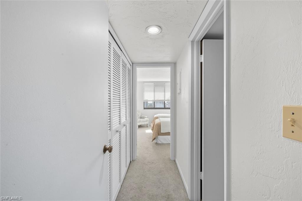 Hall with light colored carpet, a textured ceiling, and a textured wall