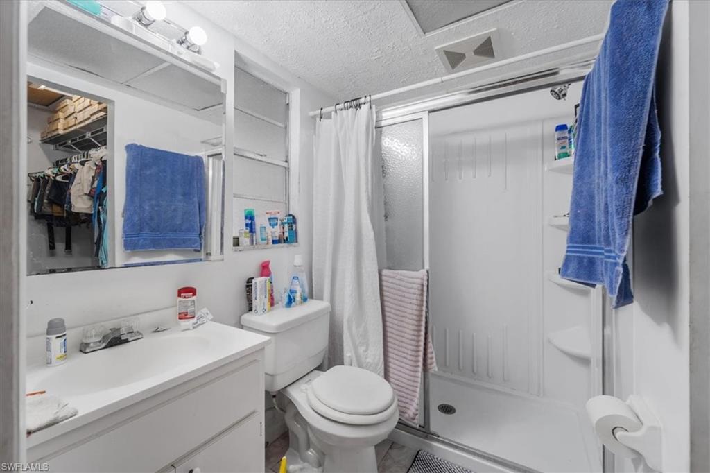 Full bath with a textured ceiling, a stall shower, vanity, and a spacious closet