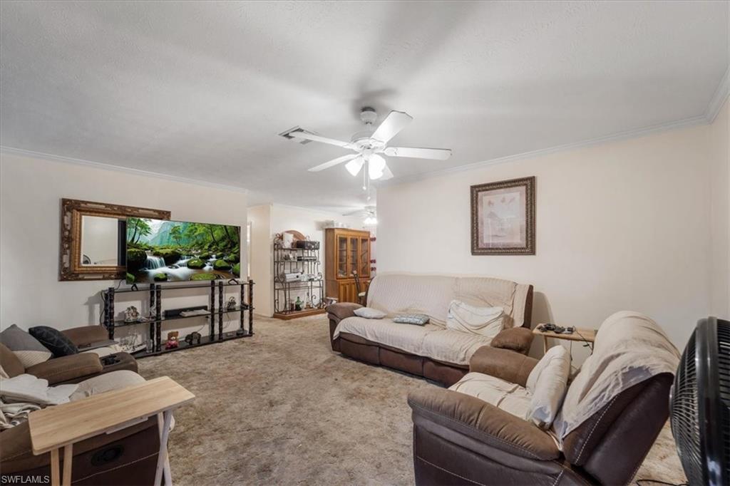 Living area featuring carpet floors, crown molding, and ceiling fan