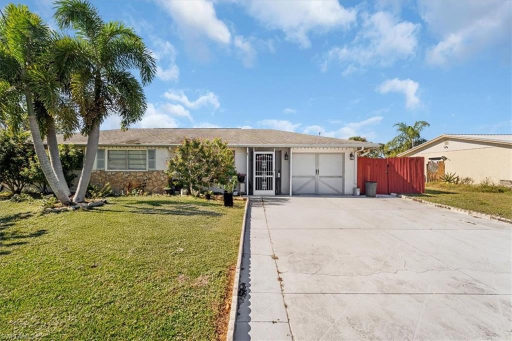 Ranch-style home featuring a front yard, driveway, an attached garage, and stone siding