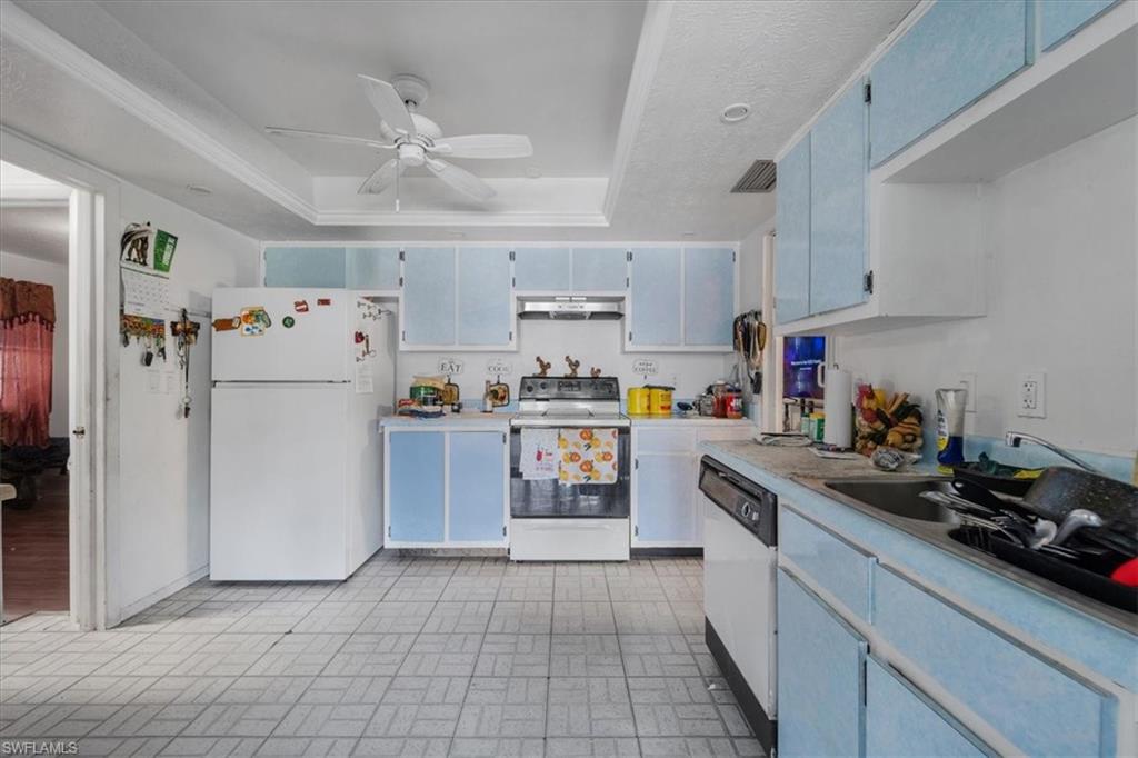 Kitchen featuring white appliances, blue cabinetry, light countertops, a tray ceiling, and brick patterned floors