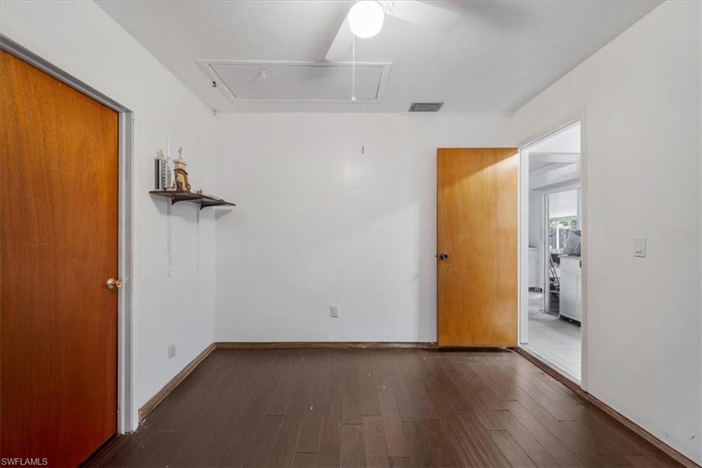 Unfurnished room featuring attic access, dark wood-style floors, and a ceiling fan