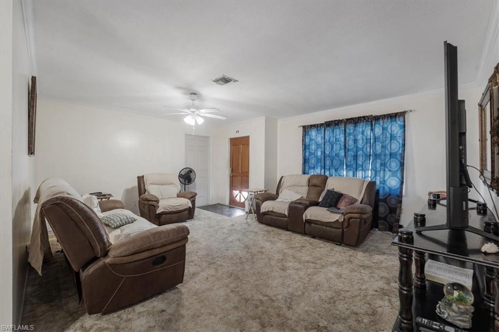 Carpeted living area with ornamental molding and ceiling fan