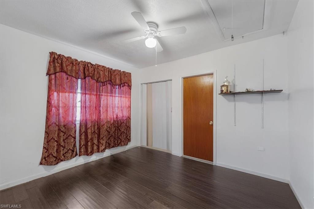 Unfurnished room featuring attic access, dark wood-style flooring, and a ceiling fan
