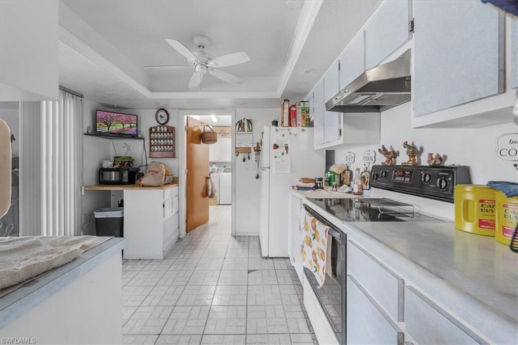 Kitchen with electric stove, a raised ceiling, under cabinet range hood, a ceiling fan, and light countertops