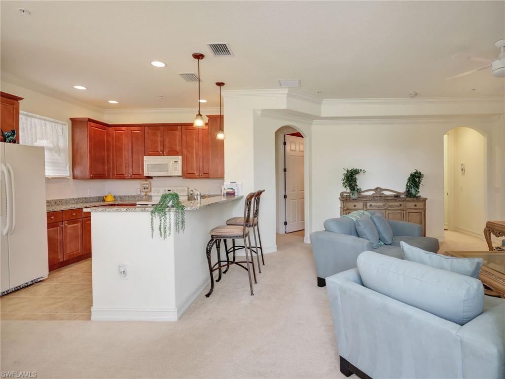 Kitchen with arched walkways, white appliances, light carpet, ornamental molding, and light stone counters