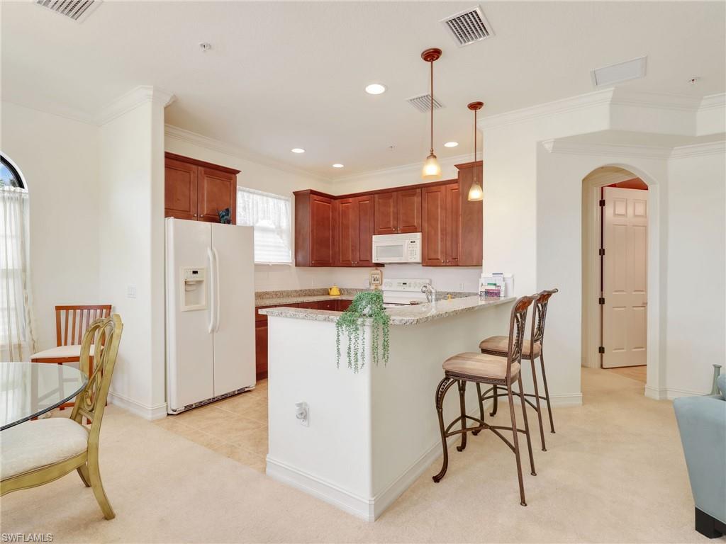 Kitchen featuring arched walkways, light colored carpet, white appliances, hanging light fixtures, and a kitchen bar