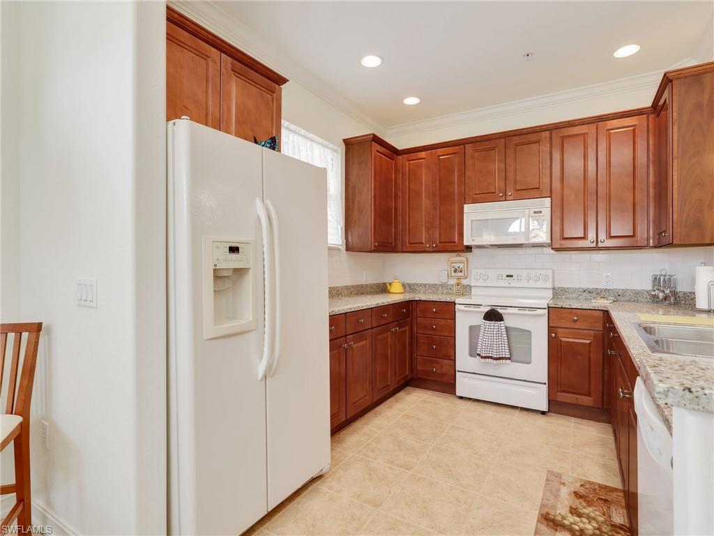 Kitchen featuring white appliances, brown cabinetry, light stone counters, ornamental molding, and recessed lighting