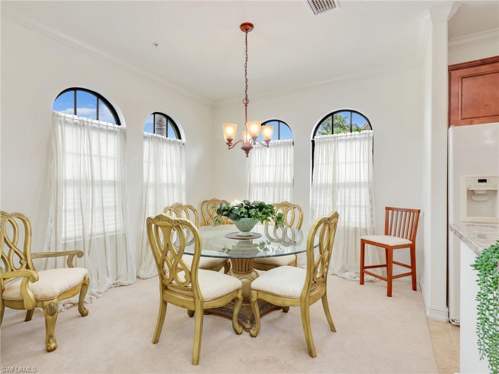 Dining space with ornamental molding, light carpet, and a chandelier