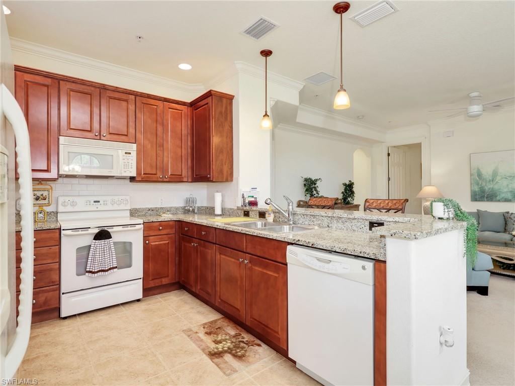 Kitchen with white appliances, hanging light fixtures, light stone counters, a peninsula, and ornamental molding