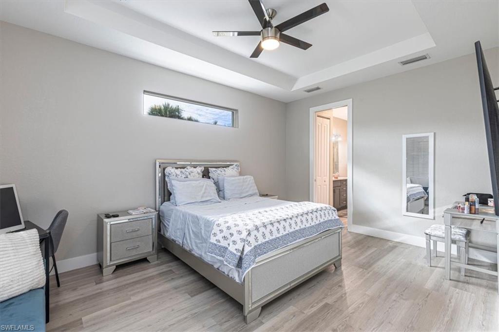 Bedroom featuring a raised ceiling, light wood-style floors, a ceiling fan, and ensuite bathroom