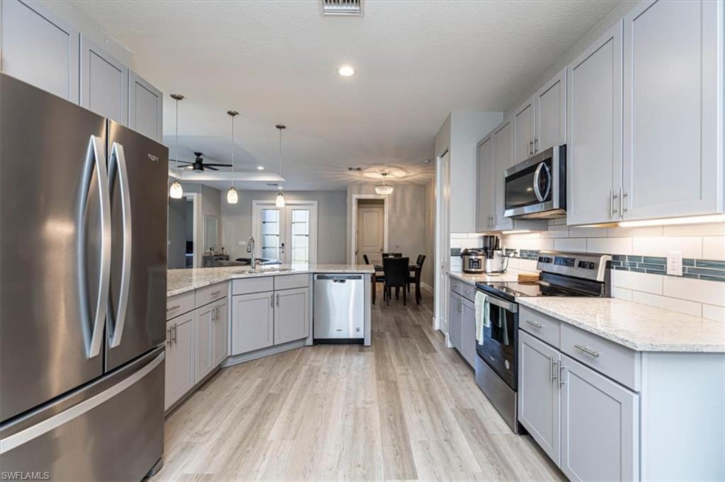 Kitchen with gray cabinets, appliances with stainless steel finishes, hanging light fixtures, light stone countertops, and recessed lighting