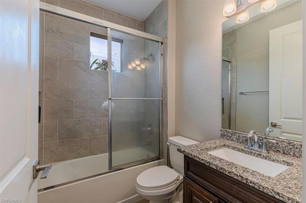 Full bathroom with vanity, bath / shower combo with glass door, and a textured wall