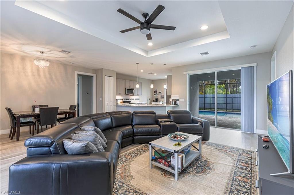 Living room featuring recessed lighting, ceiling fan, a tray ceiling, light wood-type flooring, and a chandelier