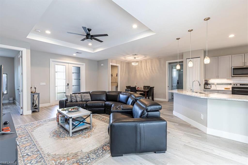 Living room featuring recessed lighting, ceiling fan, light wood-style floors, french doors, and a tray ceiling