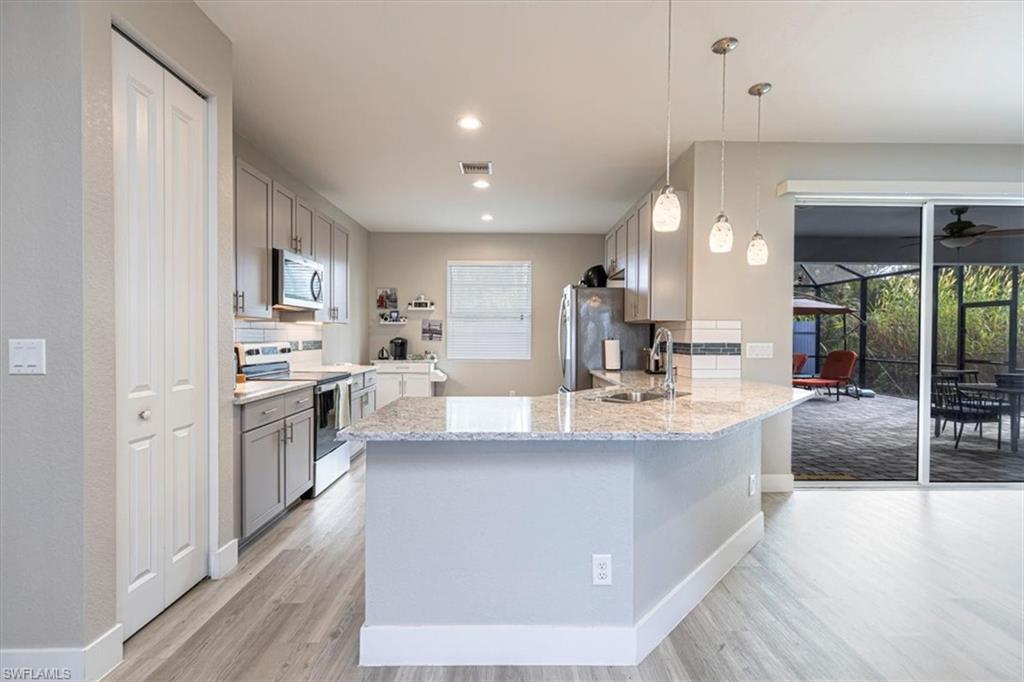 Kitchen with gray cabinetry, stainless steel appliances, light stone countertops, backsplash, and recessed lighting
