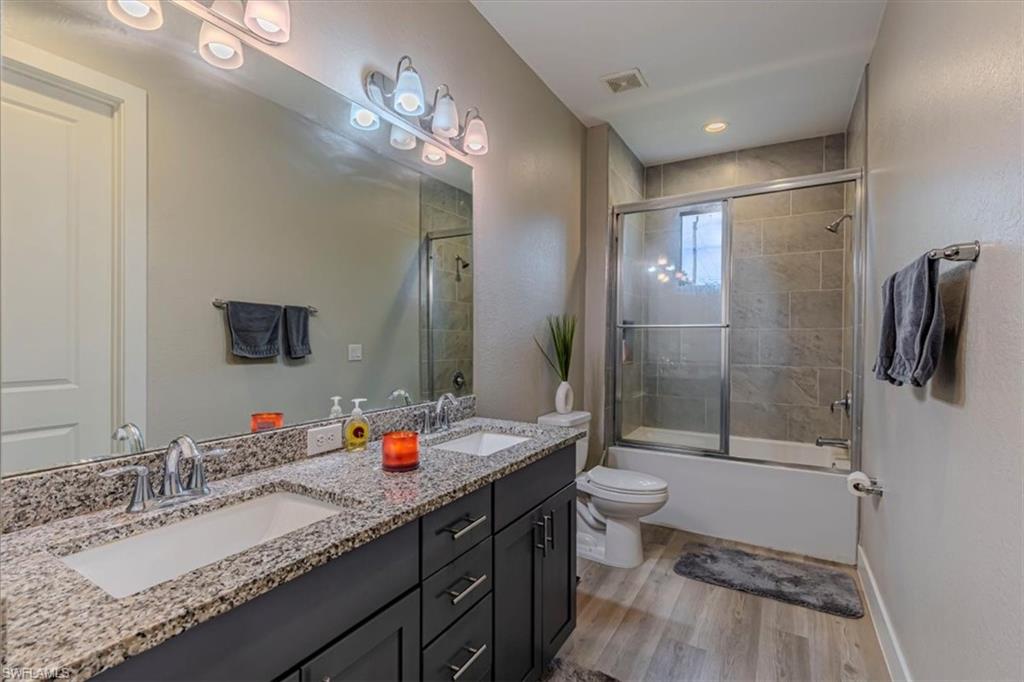 Bathroom with double vanity, light wood-type flooring, and combined bath / shower with glass door