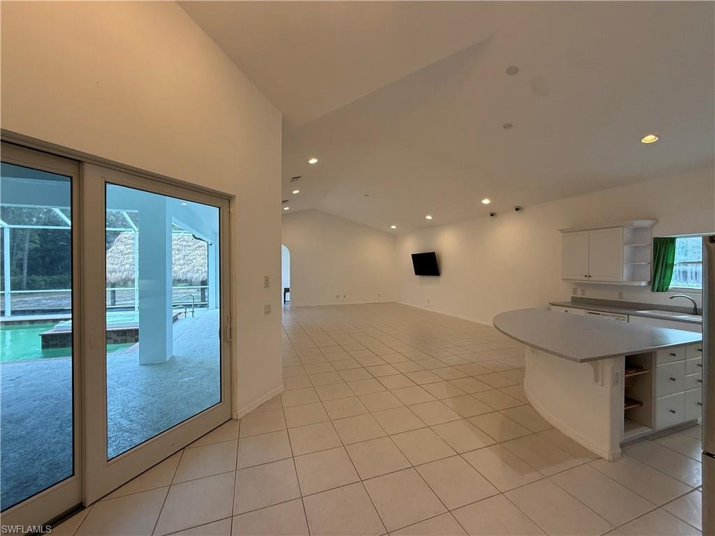 Kitchen featuring open shelves, lofted ceiling, white cabinetry, arched walkways, and open floor plan