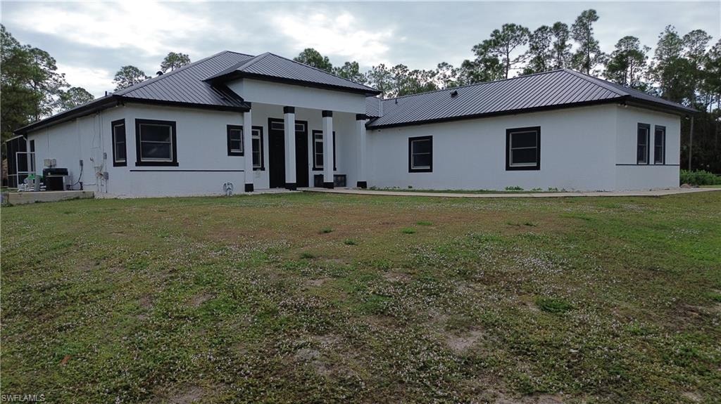 View of front facade featuring stucco siding, a front lawn, and a metal roof