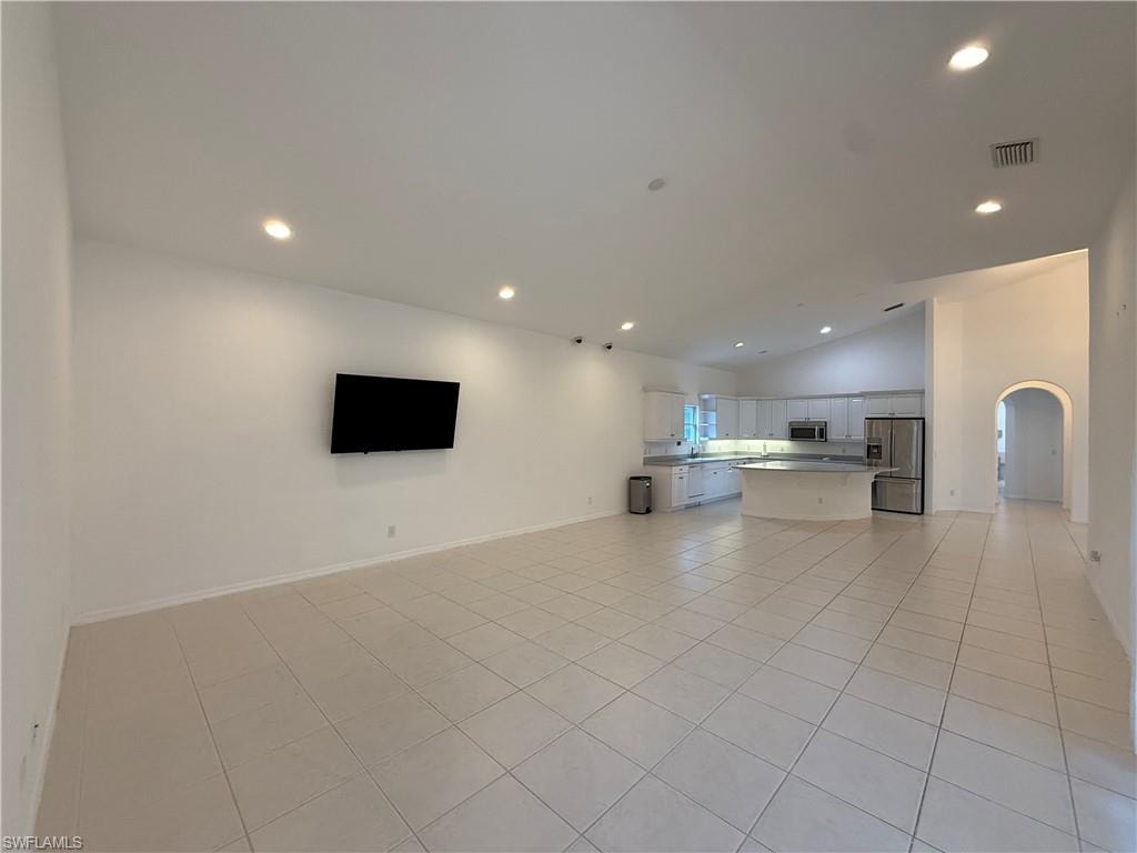 Unfurnished living room featuring arched walkways, recessed lighting, light tile patterned flooring, and high vaulted ceiling