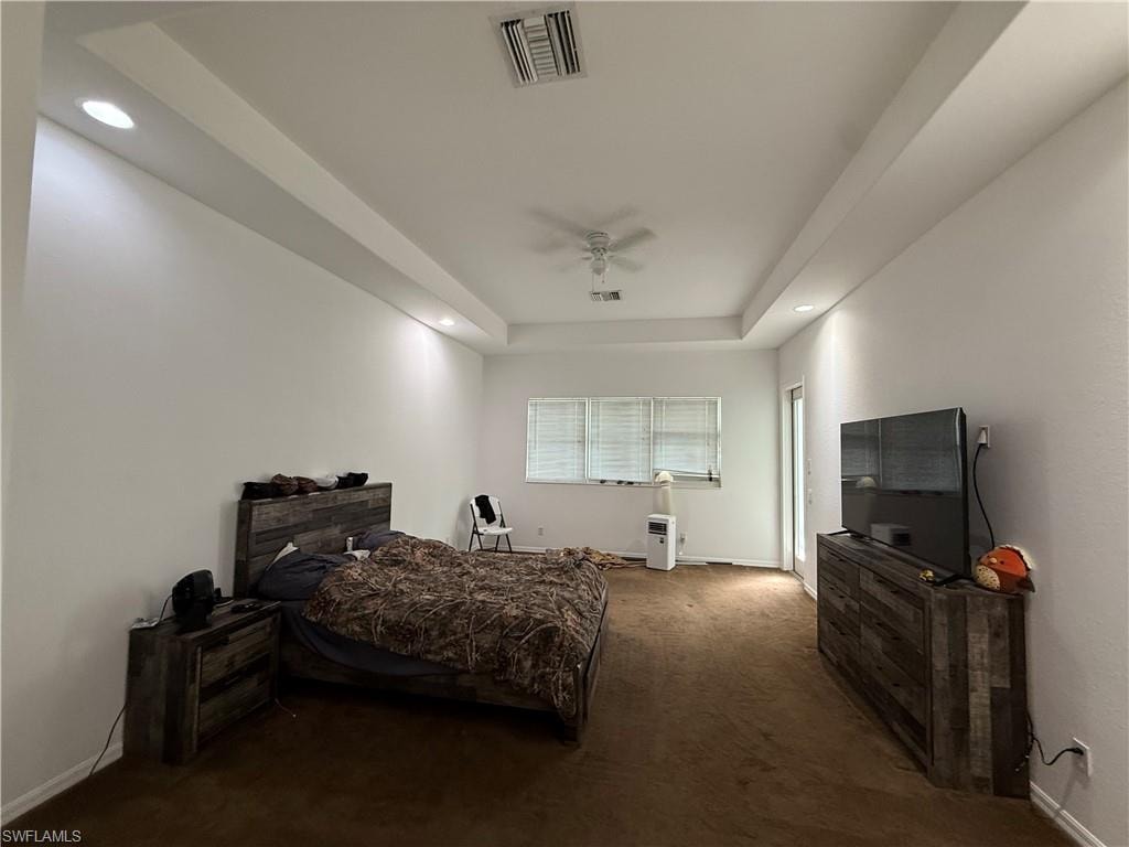 Bedroom featuring dark carpet, a tray ceiling, recessed lighting, and a ceiling fan