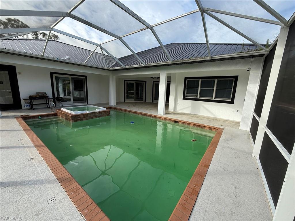 View of swimming pool featuring a sunroom, a pool with connected hot tub, a patio area, and glass enclosure