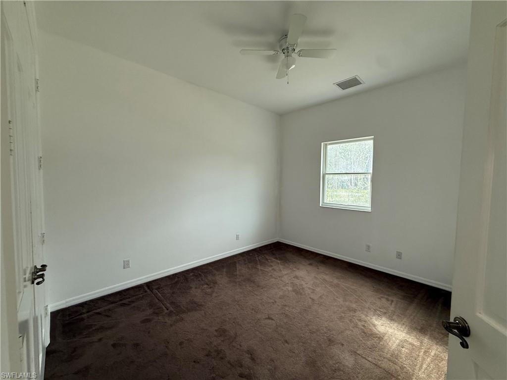 Empty room featuring dark carpet and ceiling fan