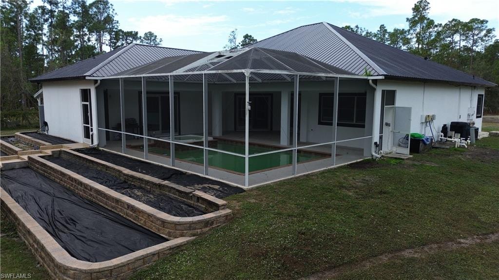 Rear view of property with a metal roof, a sunroom, and glass enclosure