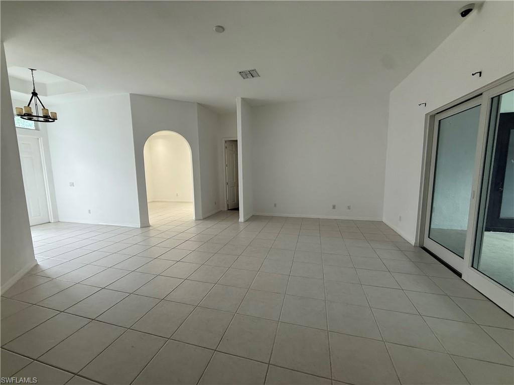 Unfurnished room featuring arched walkways, a chandelier, and light tile patterned flooring