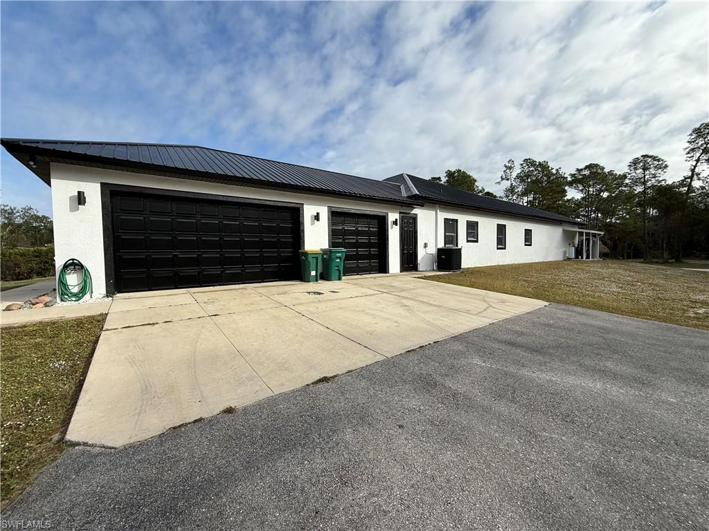 View of front of property with concrete driveway, stucco siding, a metal roof, an attached garage, and a front lawn
