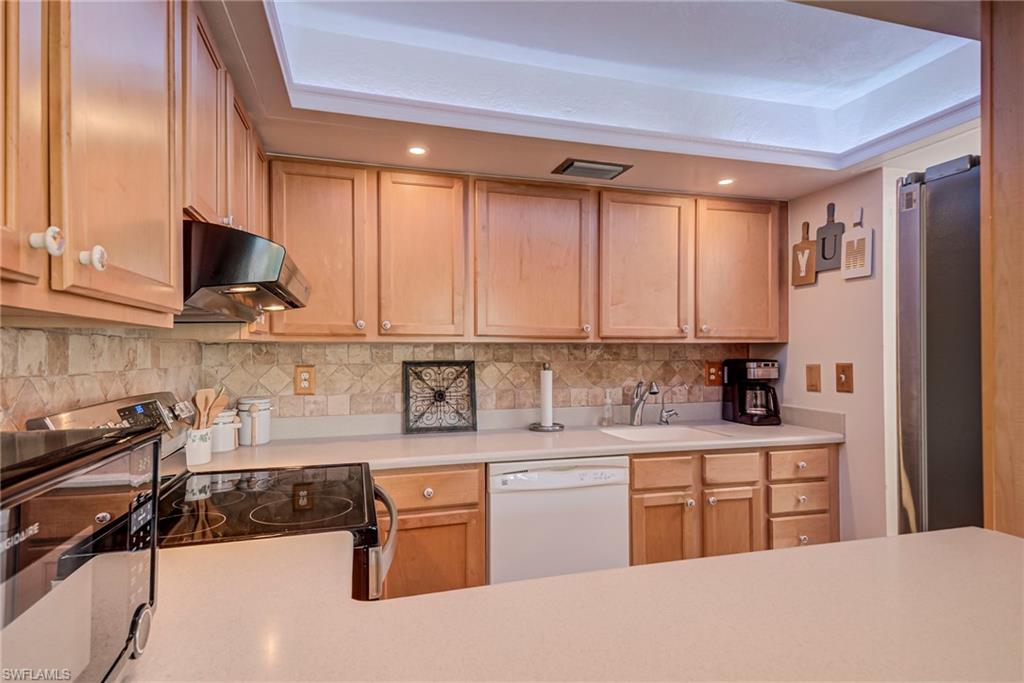 Kitchen featuring light countertops, under cabinet range hood, dishwasher, electric range, and freestanding refrigerator