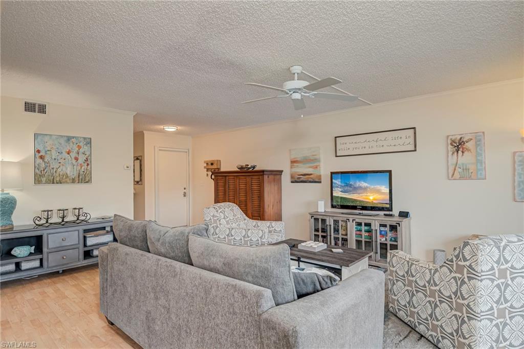 Living room with a textured ceiling, ceiling fan, and light wood-style flooring