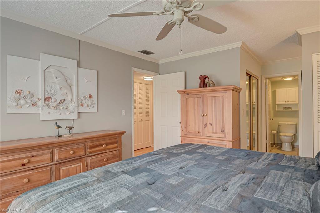 Bedroom with a textured ceiling, ensuite bath, ceiling fan, and ornamental molding