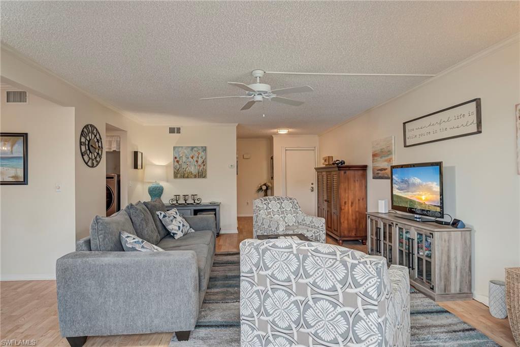 Living room featuring light wood finished floors, a textured ceiling, washer / clothes dryer, a ceiling fan, and ornamental molding