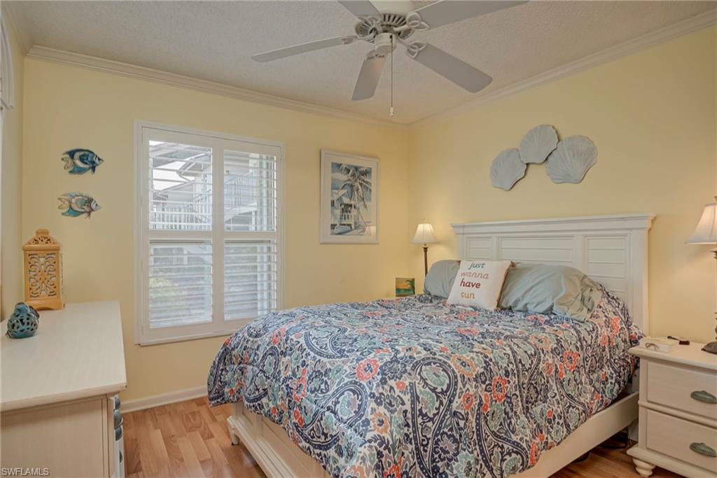 Bedroom featuring light wood-type flooring, ornamental molding, ceiling fan, and a textured ceiling