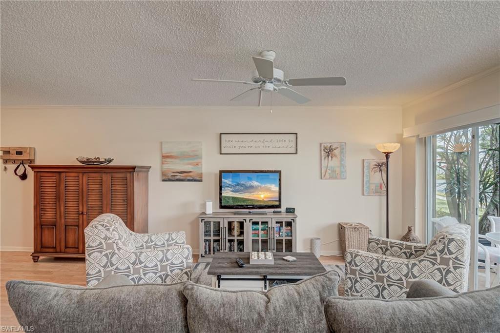 Living room with wood finished floors, ceiling fan, a textured ceiling, and crown molding