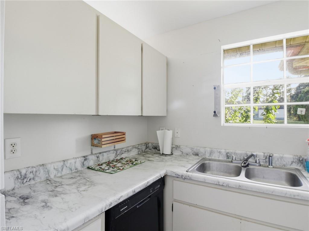 Kitchen with black dishwasher, light countertops, and white cabinetry