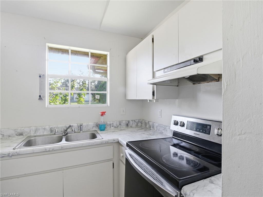 Kitchen with stainless steel electric stove, white cabinetry, and under cabinet range hood
