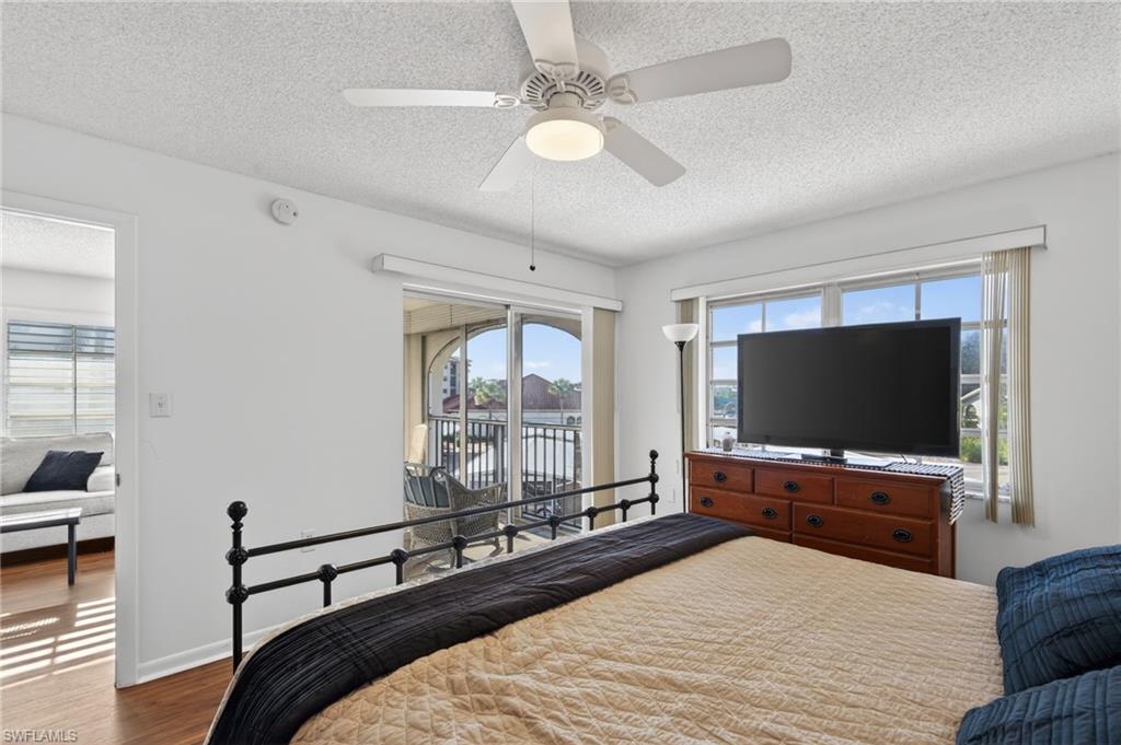 Bedroom featuring multiple windows, access to exterior, a textured ceiling, wood finished floors, and ceiling fan