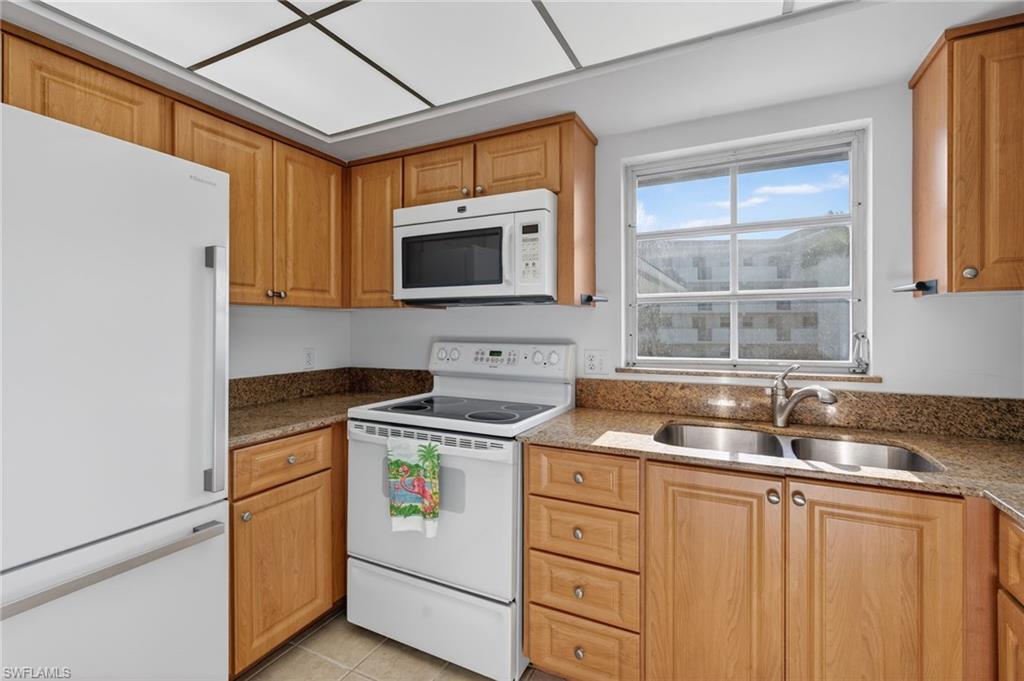 Kitchen featuring white appliances, dark stone counters, and light tile patterned flooring