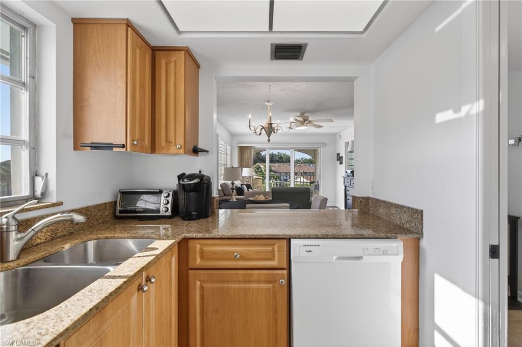 Kitchen featuring light stone countertops, white dishwasher, a chandelier, brown cabinets, and open floor plan