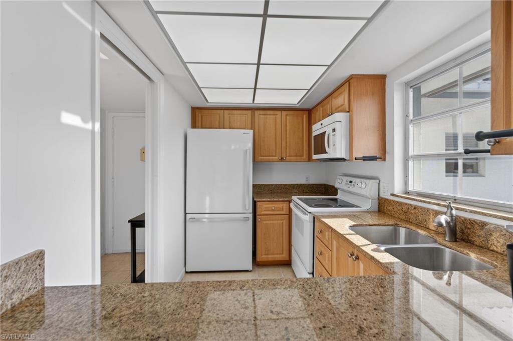 Kitchen with white appliances, light tile patterned floors, light stone countertops, and brown cabinets