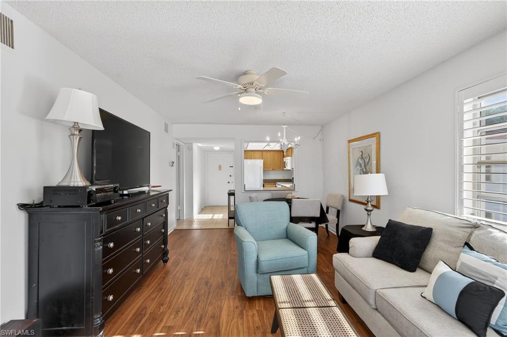 Living area featuring dark wood-type flooring, a textured ceiling, ceiling fan, and a chandelier
